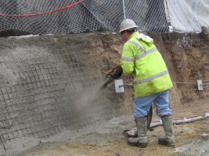 Image of shotcrete being applied over the installed helical tieback anchors within the retaining wall